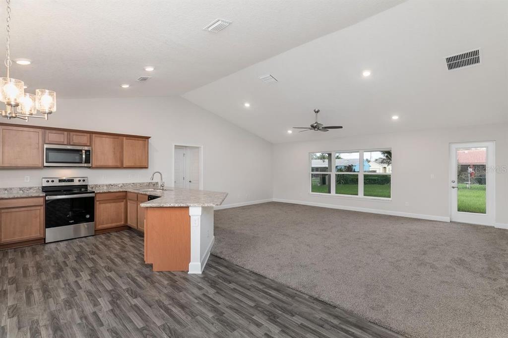 An open-concept kitchen with wood cabinets and a living area with carpet and vaulted ceilings — 21 RICHMOND DRIVE, PALM COAST, FL