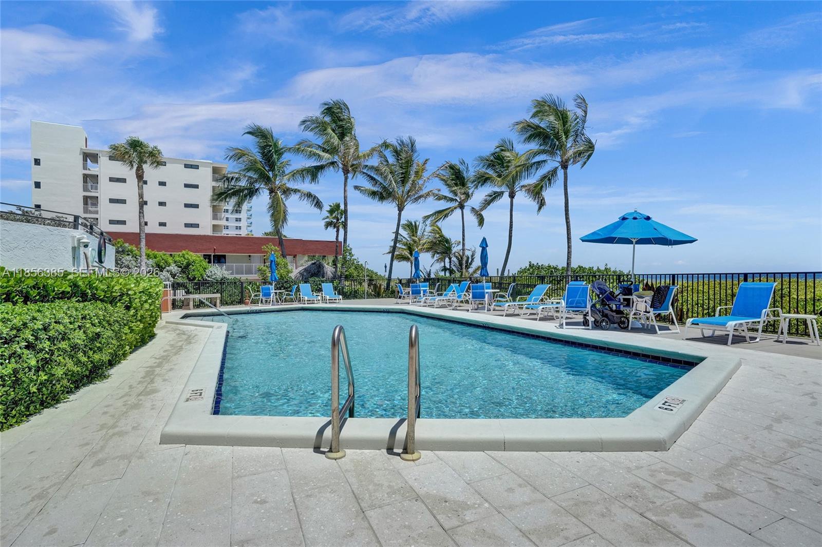 A swimming pool with lounge chairs and palm trees sits on a sunny patio — 1500 N Ocean Blvd # 801, Pompano Beach FL 33062, POMPANO BEACH, FL