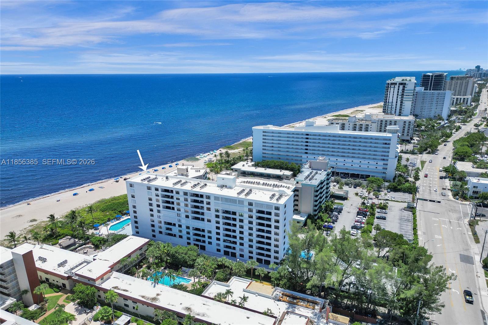 An aerial view shows a white beachfront condominium building with a pool and parking lot — 1500 N Ocean Blvd # 801, Pompano Beach FL 33062, POMPANO BEACH, FL