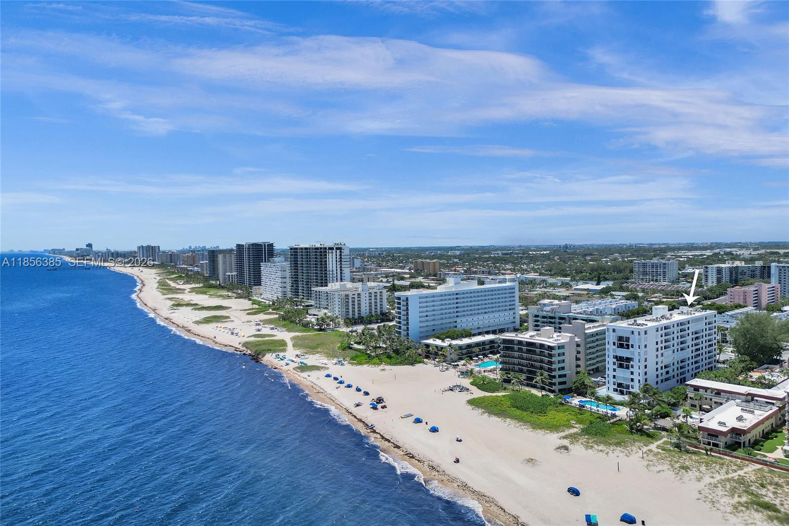 An aerial view shows a white beachfront apartment building marked with a white arrow — 1500 N Ocean Blvd # 801, Pompano Beach FL 33062, POMPANO BEACH, FL