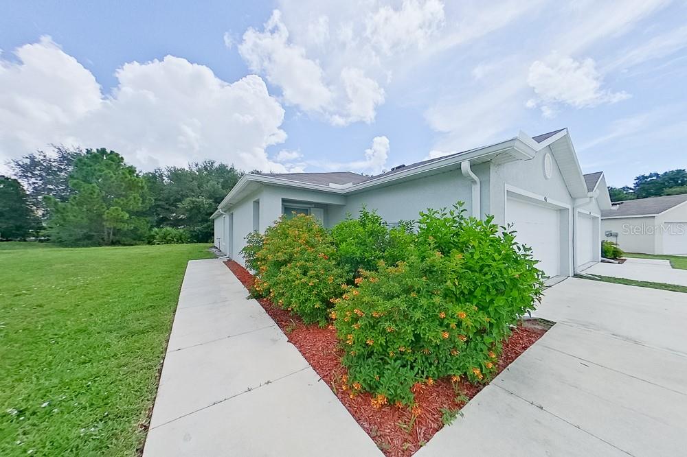 A single-story house exterior features a concrete driveway, a sidewalk, and a landscaped garden bed — 9141 AEGEAN CIRCLE, LEHIGH ACRES, FL