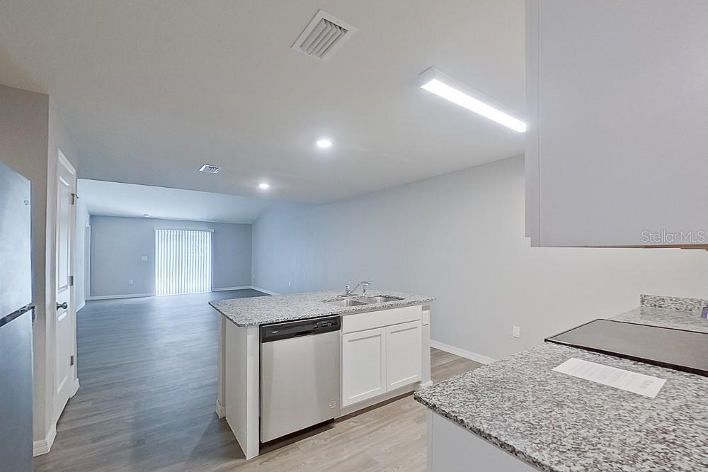 A kitchen with granite countertops and stainless steel appliances overlooks an open living area — 9141 AEGEAN CIRCLE, LEHIGH ACRES, FL
