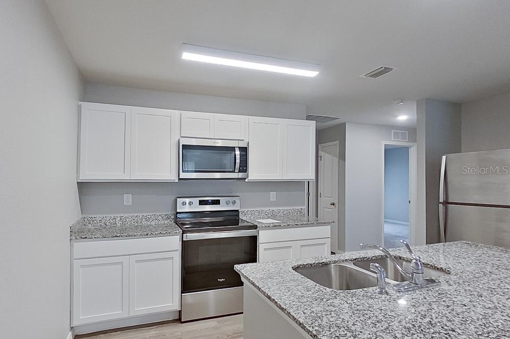 A kitchen features white cabinets, granite countertops, stainless steel appliances, and a central island sink — 9141 AEGEAN CIRCLE, LEHIGH ACRES, FL