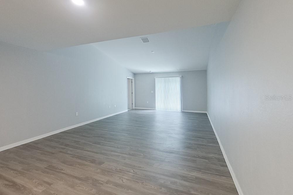An empty living room features light gray walls, wood-look flooring, and a sliding glass door — 9141 AEGEAN CIRCLE, LEHIGH ACRES, FL