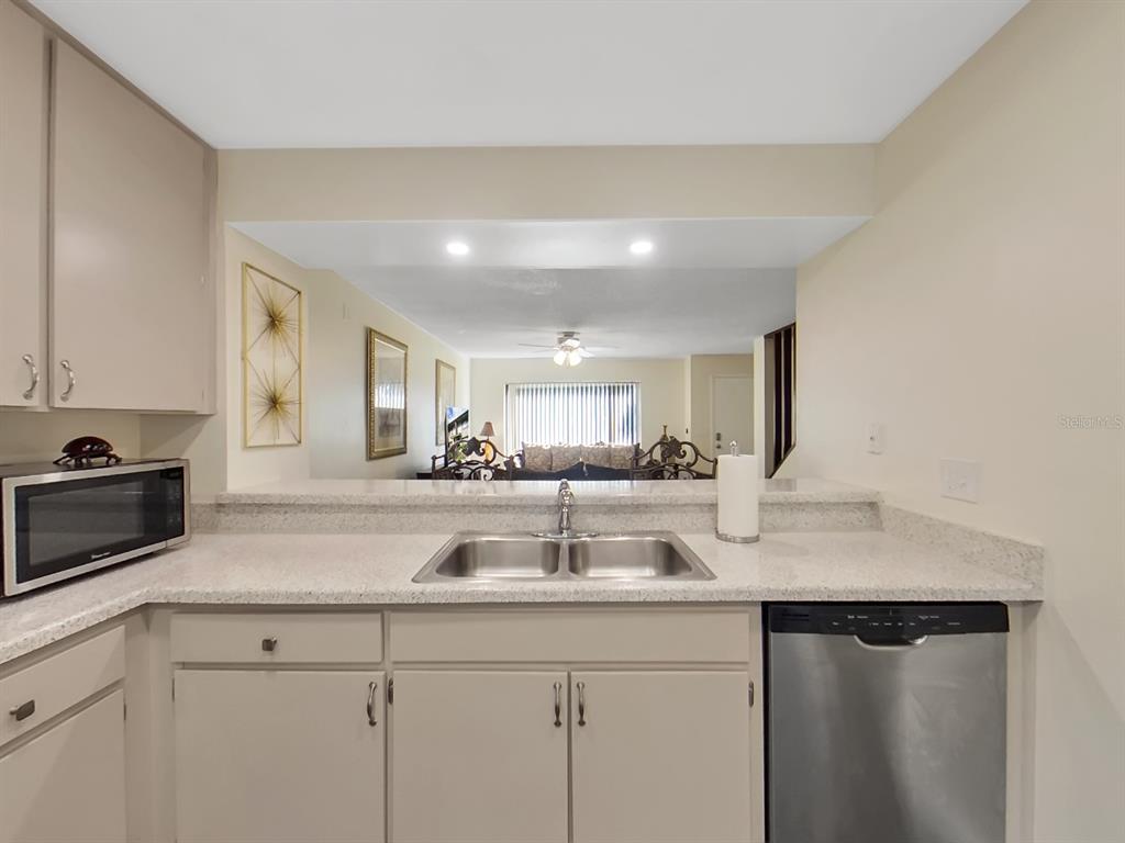 A kitchen with light-colored cabinets, a stainless steel dishwasher, and a pass-through to the living room — 7805 AMBERLEA COURT, TEMPLE TERRACE, FL