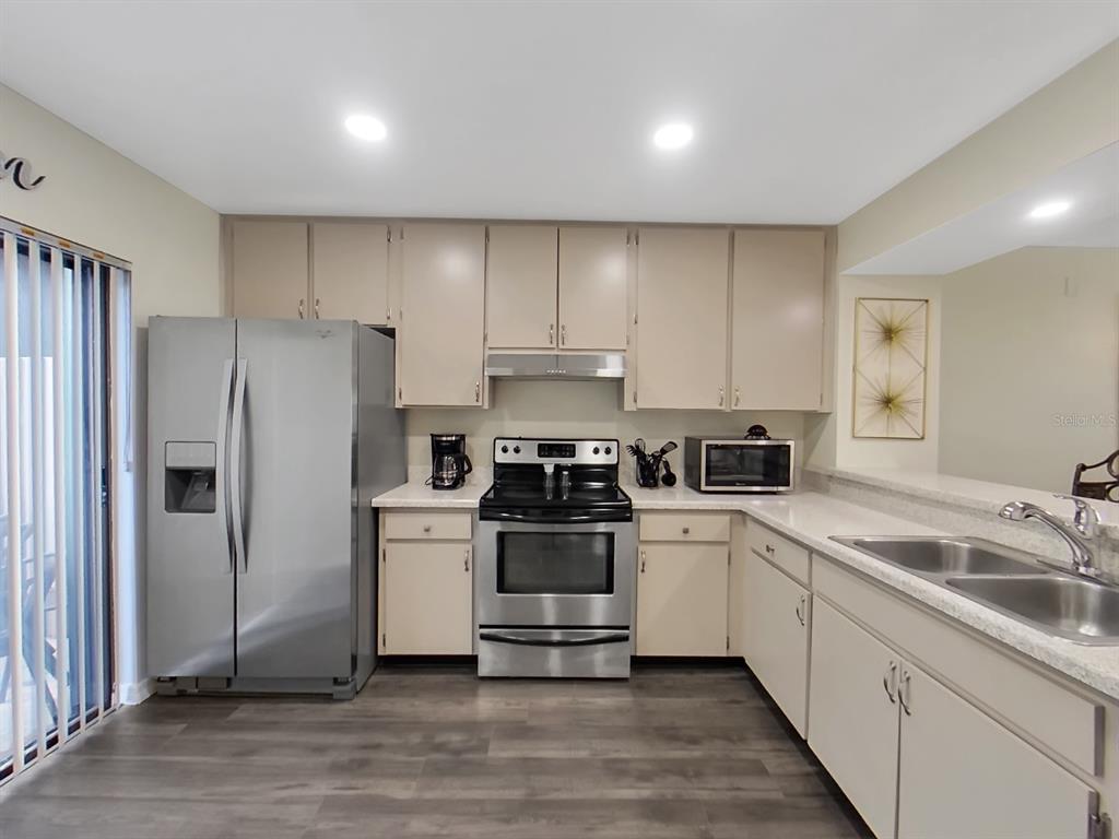 A kitchen features beige cabinets, stainless steel appliances, white countertops, and gray wood-look flooring — 7805 AMBERLEA COURT, TEMPLE TERRACE, FL
