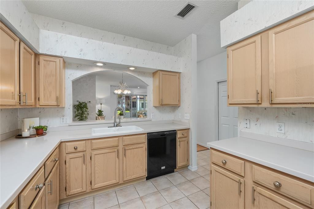 A kitchen features light wood cabinets, white countertops, a black dishwasher, and a pass-through window — 3511 TEALWOOD CIRCLE, PALM HARBOR, FL