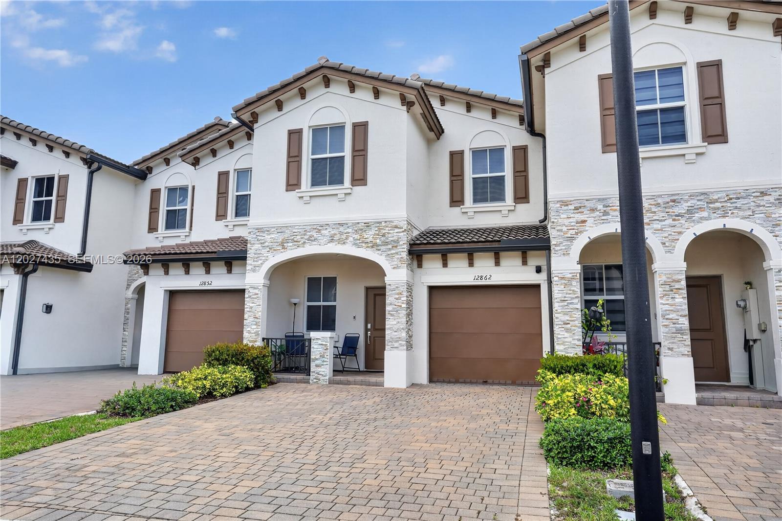 A two-story townhouse exterior features a stone facade, brown garage doors, and a paved driveway — 12862 NW 23rd Pl, Miami FL 33167, MIAMI, FL