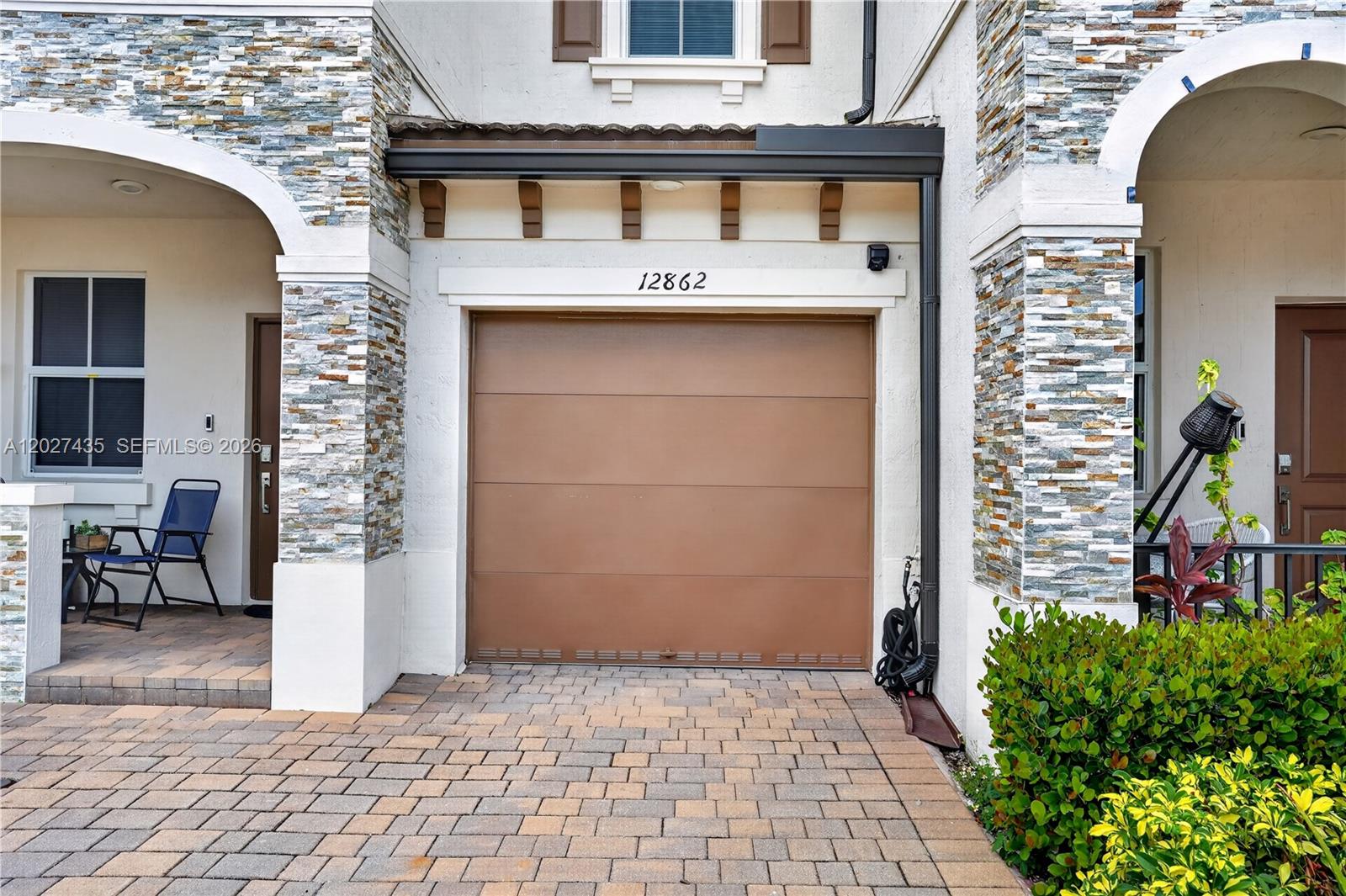A brown garage door is centered between stone-accented pillars and a paved driveway — 12862 NW 23rd Pl, Miami FL 33167, MIAMI, FL