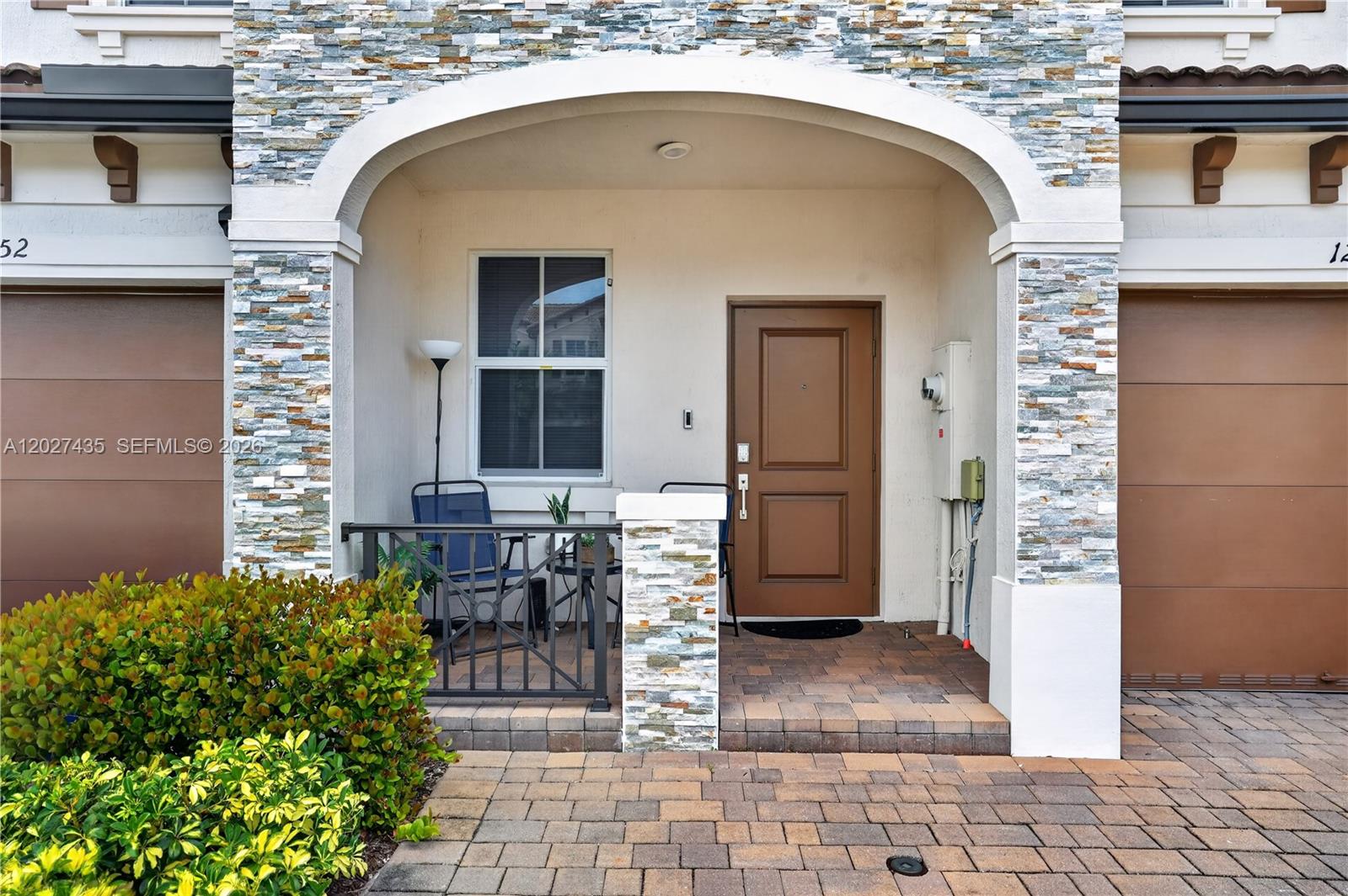 The exterior of a home features a stone-faced arched entryway, a brown door, and pavers — 12862 NW 23rd Pl, Miami FL 33167, MIAMI, FL
