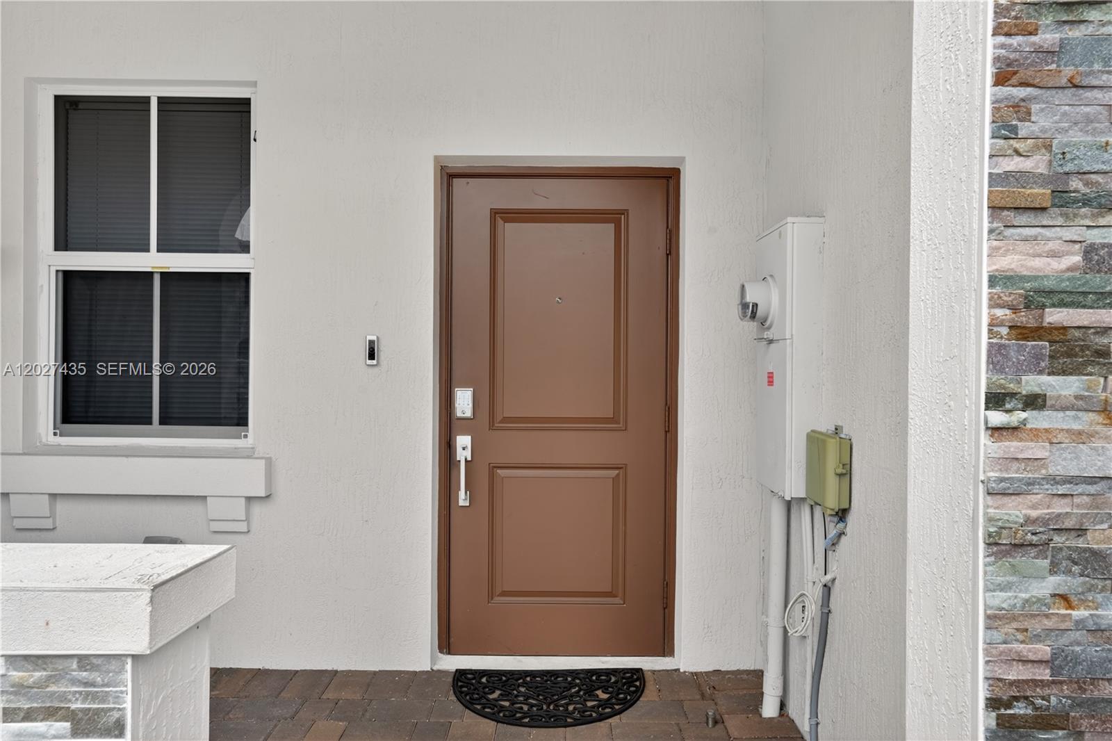 A brown front door with a keypad lock sits beside a window and utility box — 12862 NW 23rd Pl, Miami FL 33167, MIAMI, FL