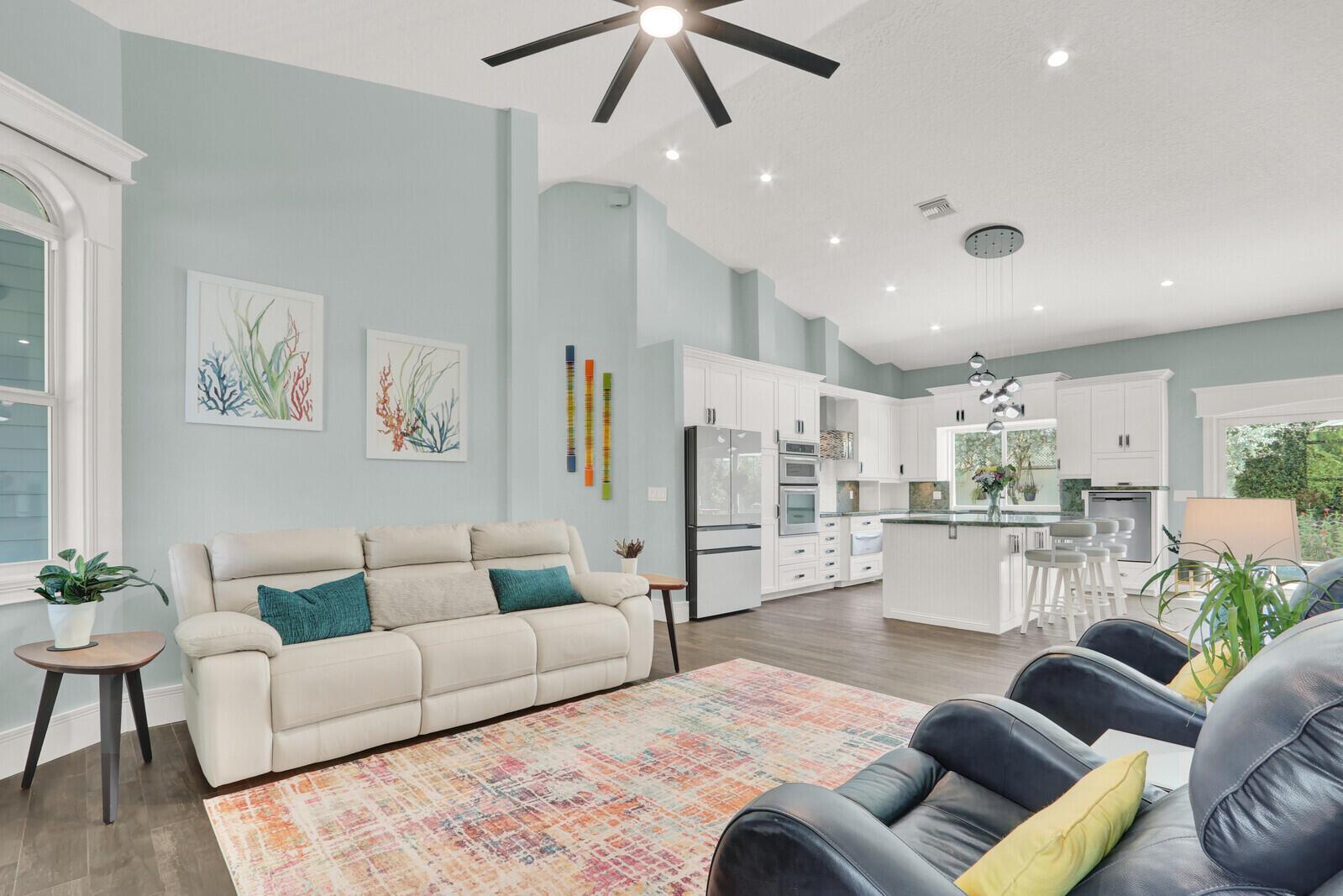 An open-concept living room and kitchen featuring light blue walls, white cabinetry, and a rug — 119 Faith Way, Jupiter FL 33458, JUPITER, FL