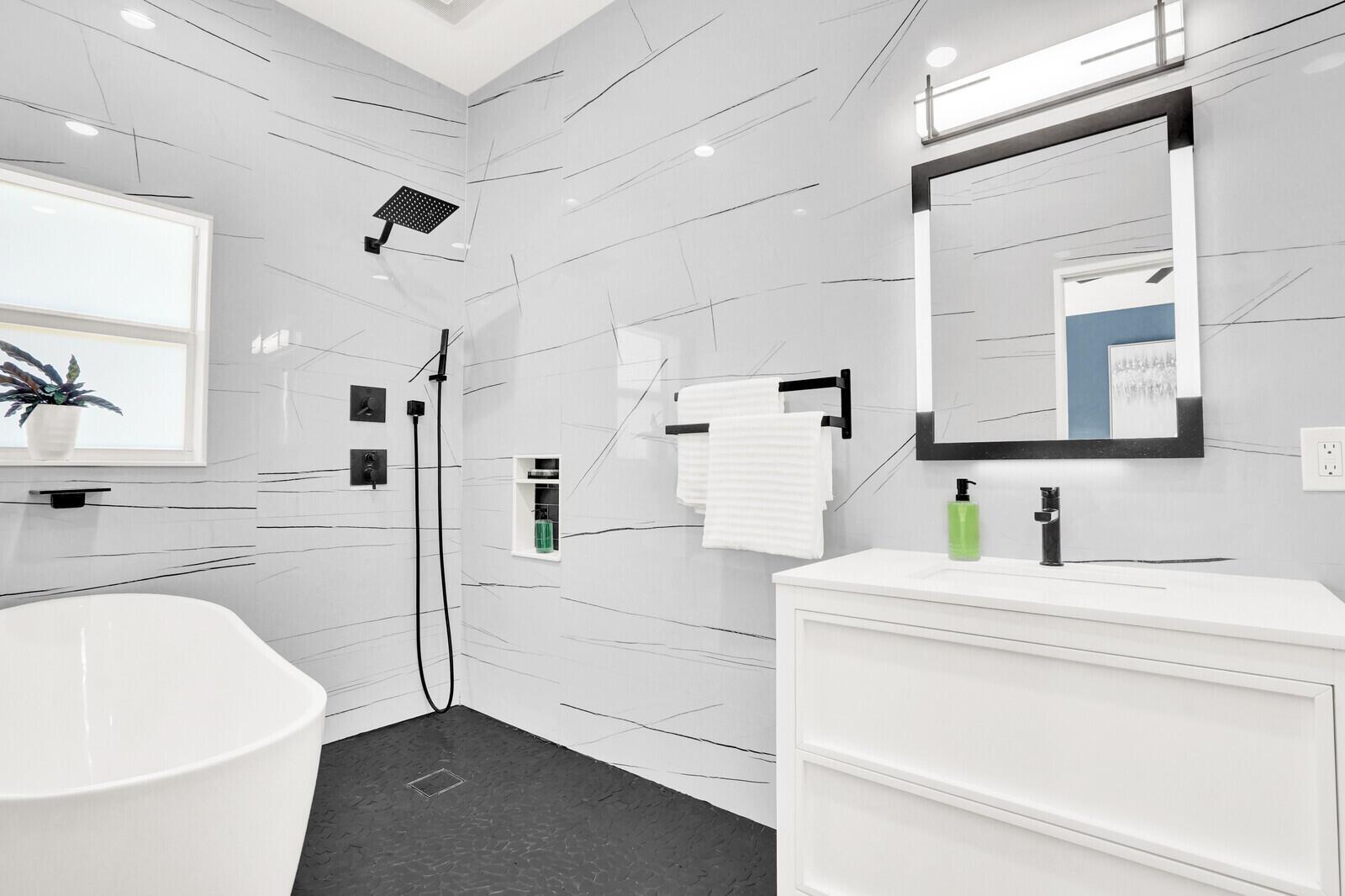 A modern bathroom features a white soaking tub, black fixtures, and light gray veined tile — 119 Faith Way, Jupiter FL 33458, JUPITER, FL