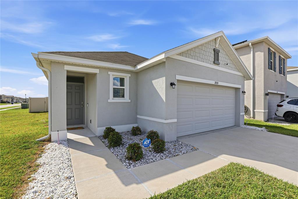 A single-story house with a gray exterior, a two-car garage, and a small landscaped garden — 2839 MAIDEN GRASS ISLE, WESLEY CHAPEL, FL
