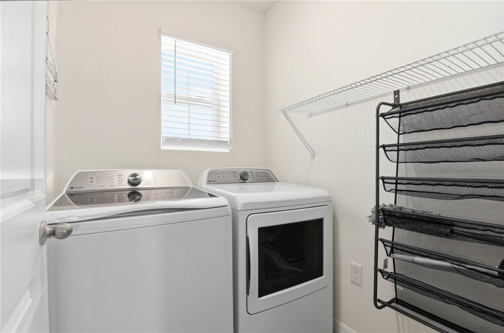 A laundry room features a white washer and dryer, a window, and wall-mounted storage shelving — 2839 MAIDEN GRASS ISLE, WESLEY CHAPEL, FL