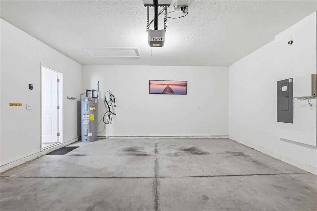 A garage with a concrete floor, a water heater, an EV charger, and an electrical panel — 2839 MAIDEN GRASS ISLE, WESLEY CHAPEL, FL