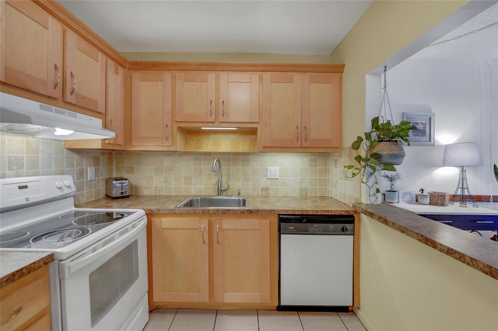 A kitchen features light wood cabinets, a white stove, a dishwasher, and a tiled backsplash — 257 S Cypress Road # 401, Pompano Beach FL 33060, POMPANO BEACH, FL