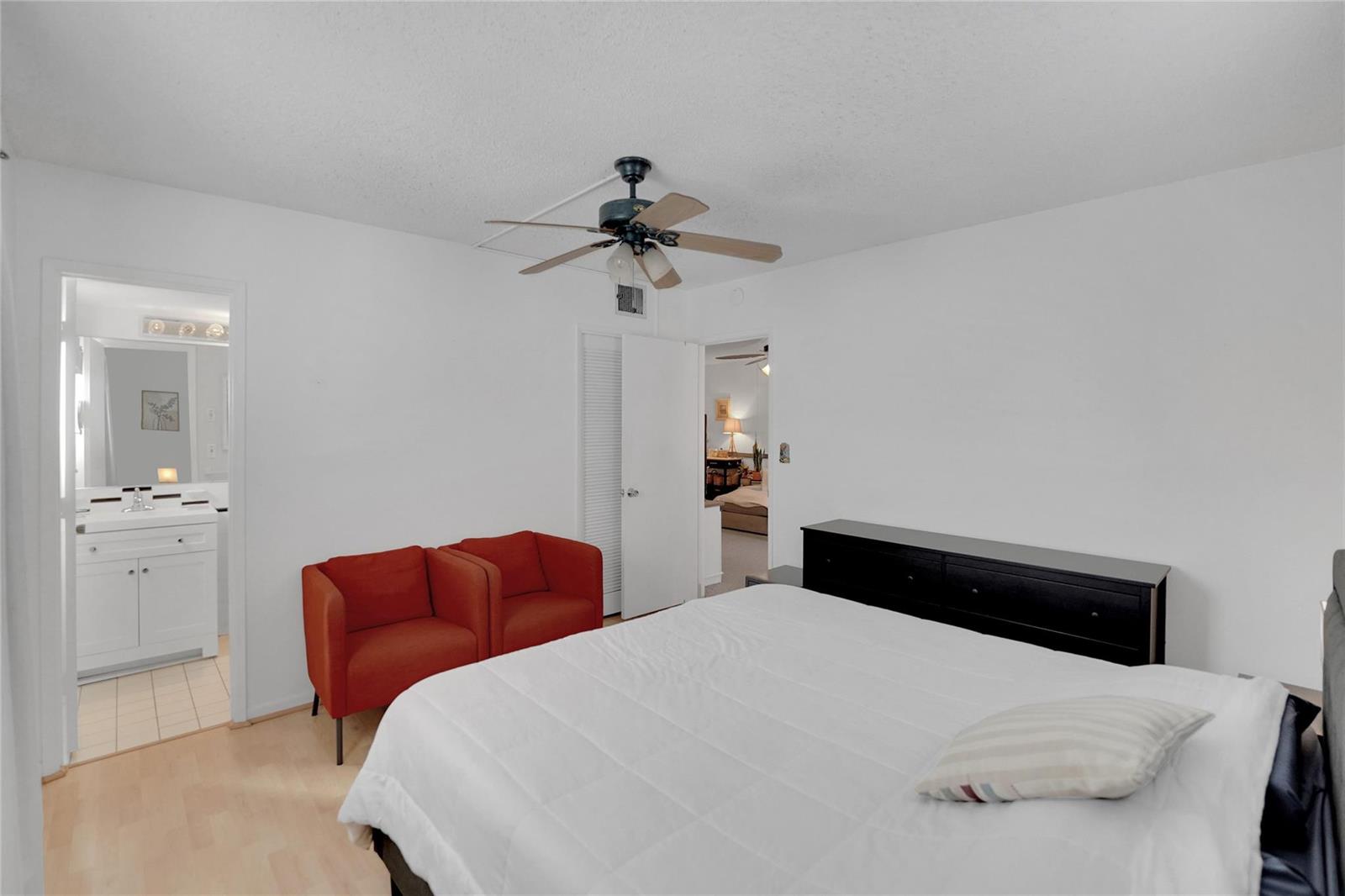 A bedroom features a bed, two orange chairs, a black dresser, and an attached bathroom — 257 S Cypress Road # 401, Pompano Beach FL 33060, POMPANO BEACH, FL