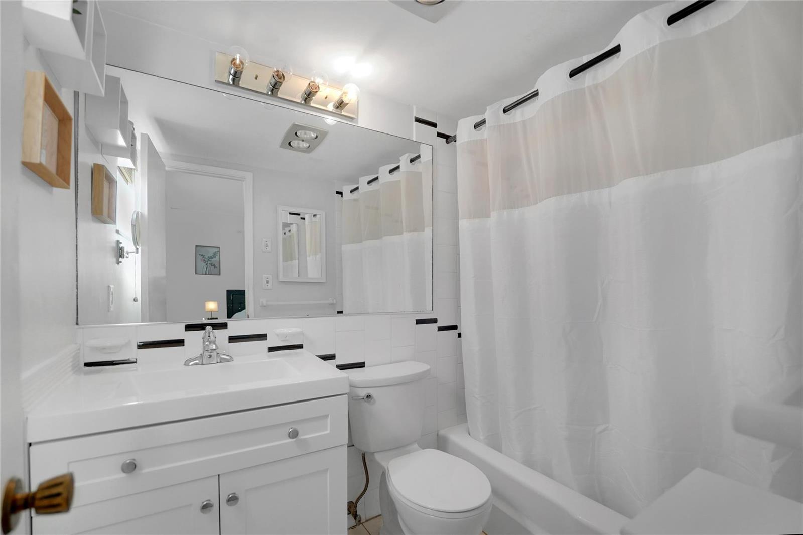 A white bathroom features a vanity, toilet, and a shower-tub combination with a curtain — 257 S Cypress Road # 401, Pompano Beach FL 33060, POMPANO BEACH, FL