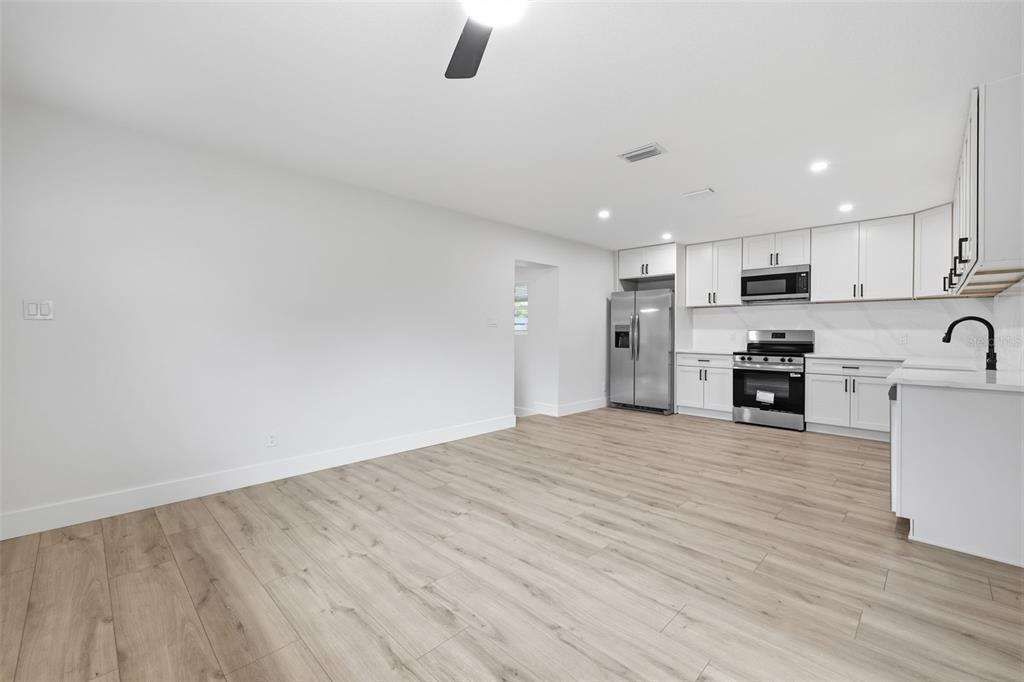 A modern kitchen with white cabinets and stainless steel appliances opens to a living area — 4409 W WYOMING AVENUE, TAMPA, FL