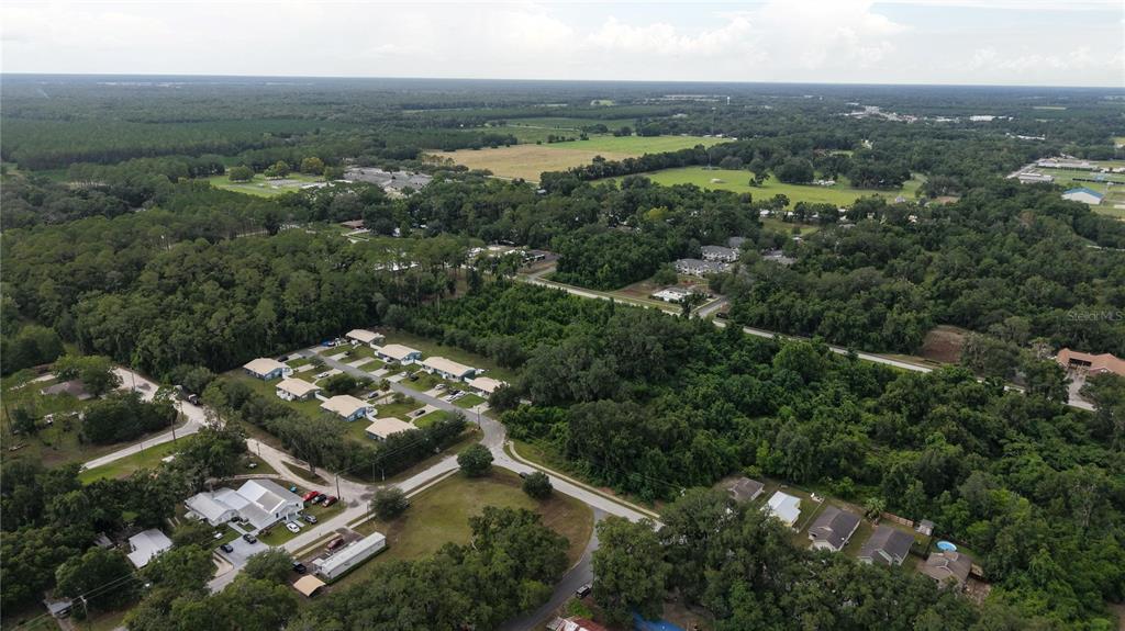 An aerial view shows a residential neighborhood surrounded by dense forest and open fields — SW 2ND AVENUE, CHIEFLAND, FL