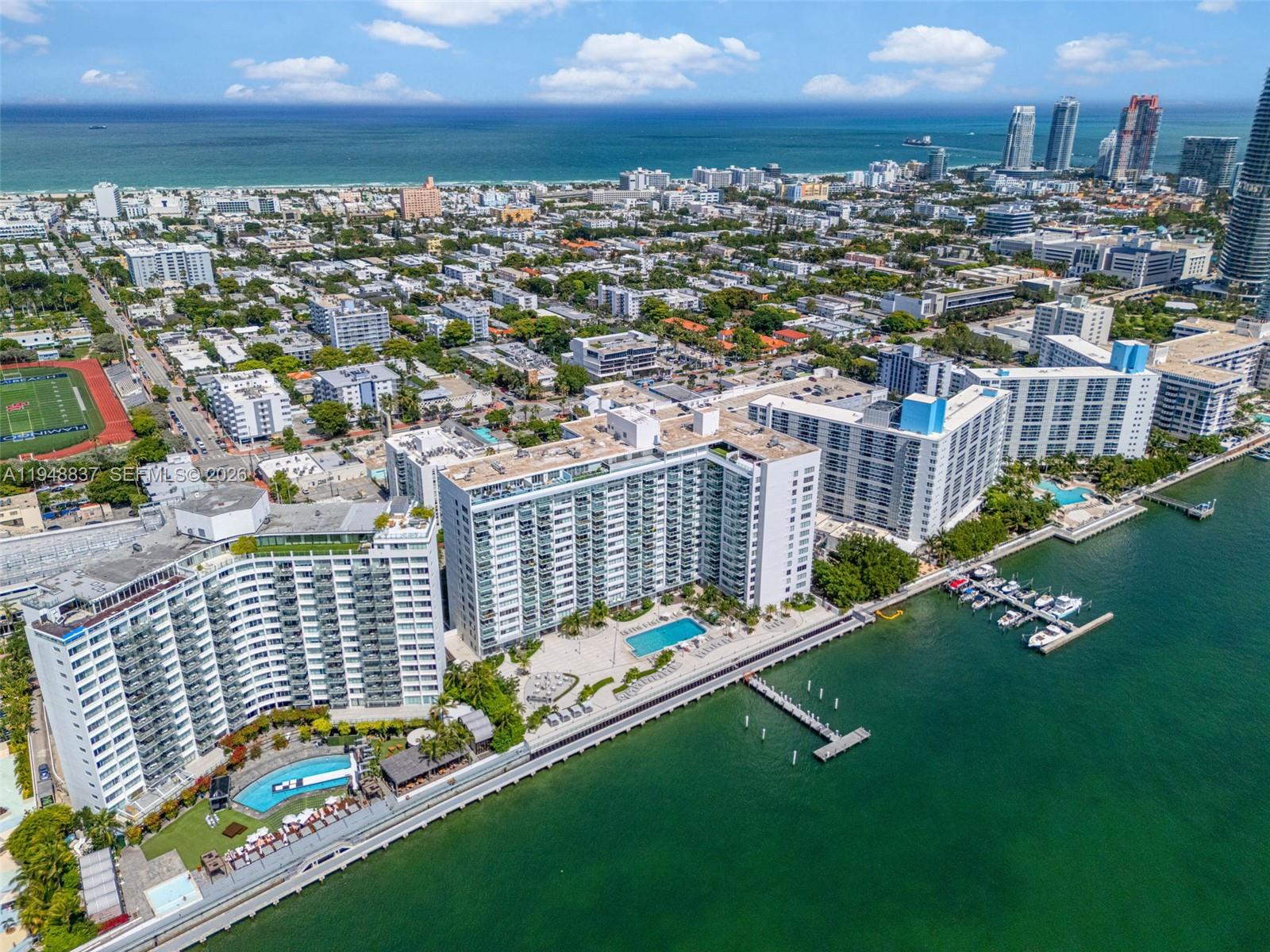 An aerial view shows several large waterfront apartment buildings with pools and a boat dock — 1000 West Ave # 609, Miami Beach FL 33139, MIAMI BEACH, FL