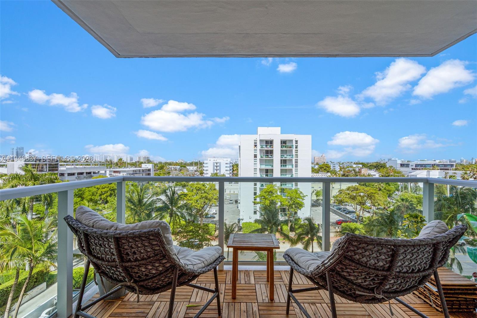 A balcony features two wicker chairs, a small wooden table, and a view of buildings — 1000 West Ave # 609, Miami Beach FL 33139, MIAMI BEACH, FL
