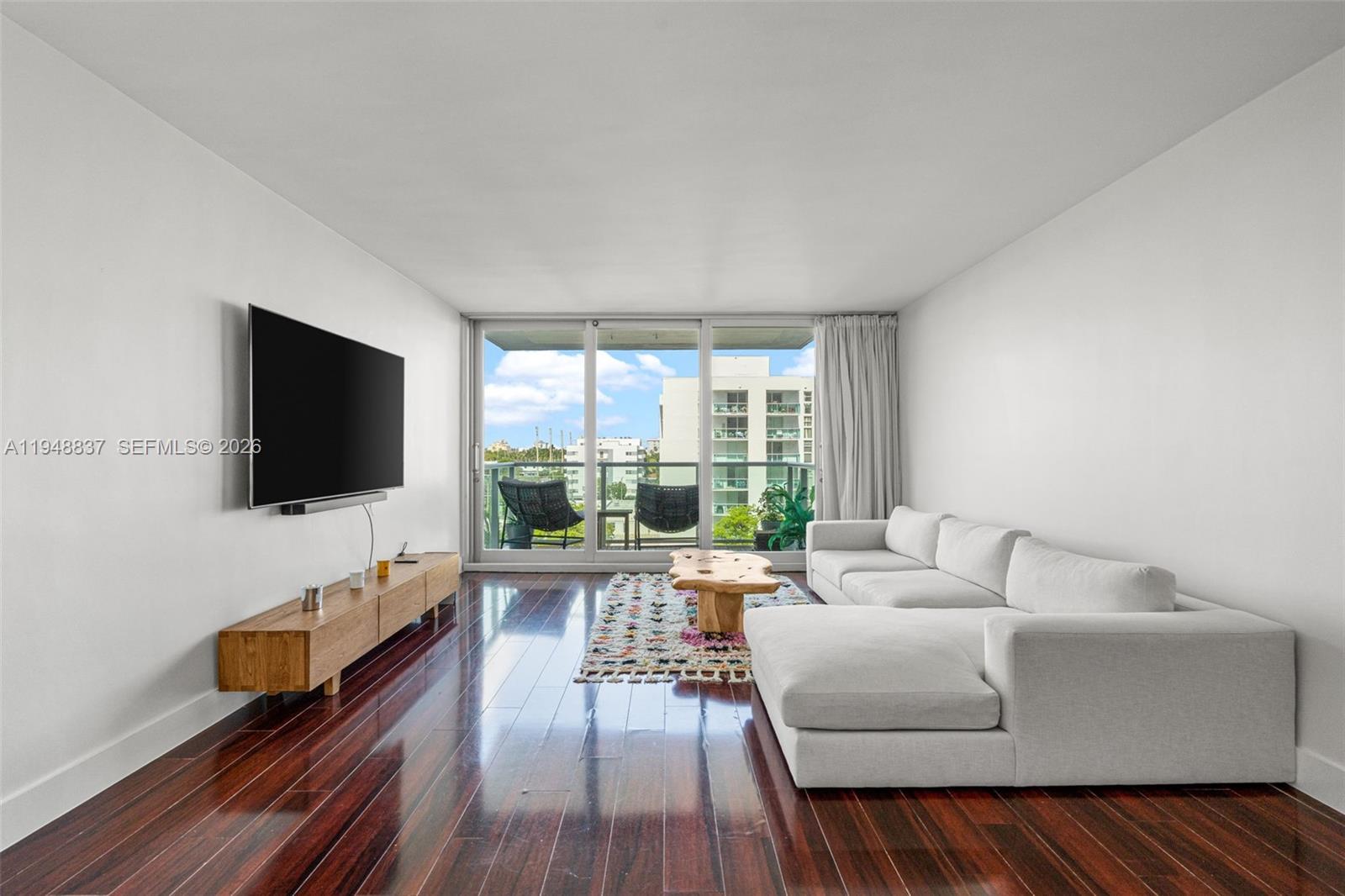A living room features dark hardwood floors, a white sectional sofa, and a balcony view — 1000 West Ave # 609, Miami Beach FL 33139, MIAMI BEACH, FL