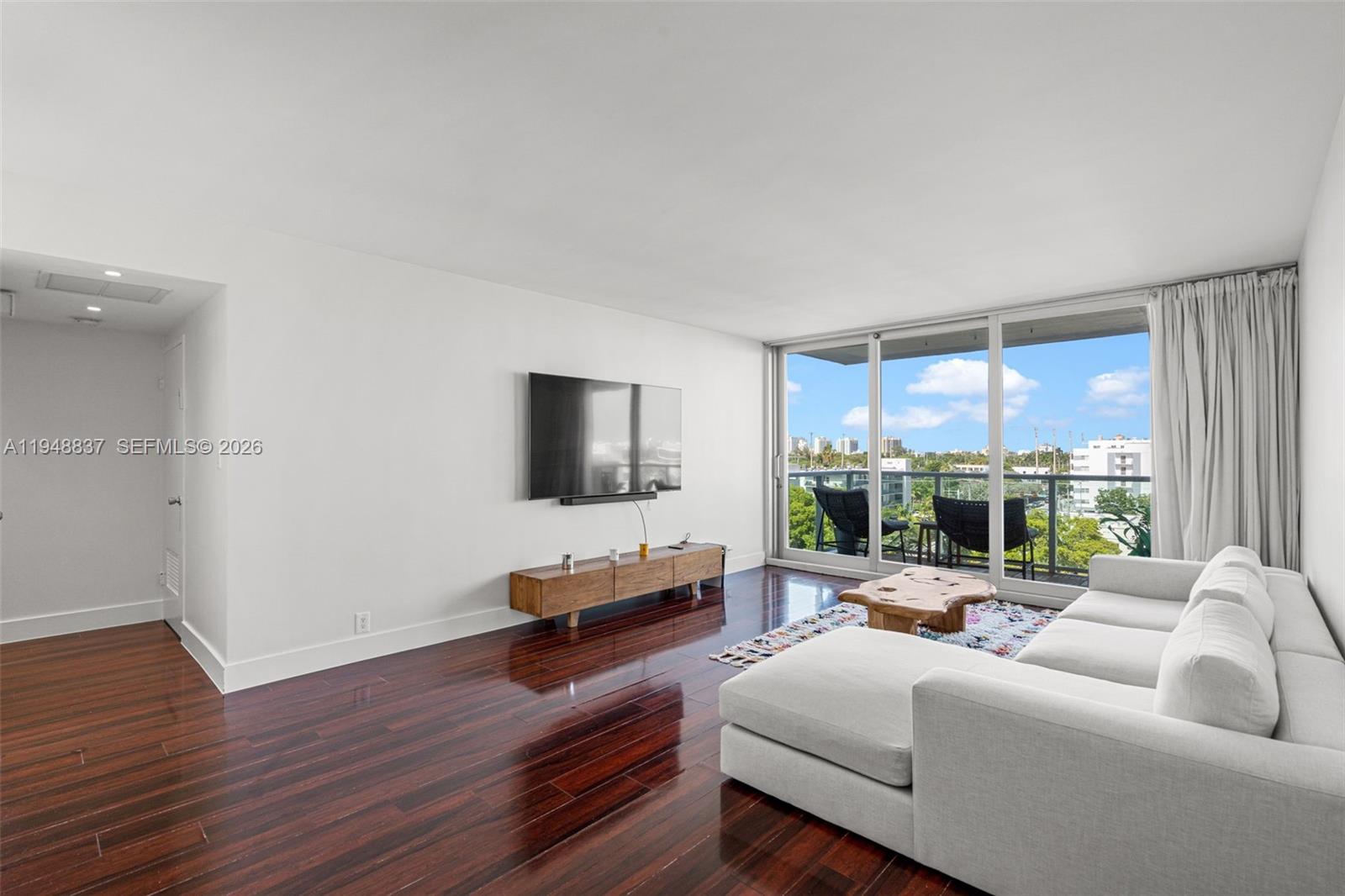 A living room features dark wood floors, a white sectional sofa, and a balcony view — 1000 West Ave # 609, Miami Beach FL 33139, MIAMI BEACH, FL
