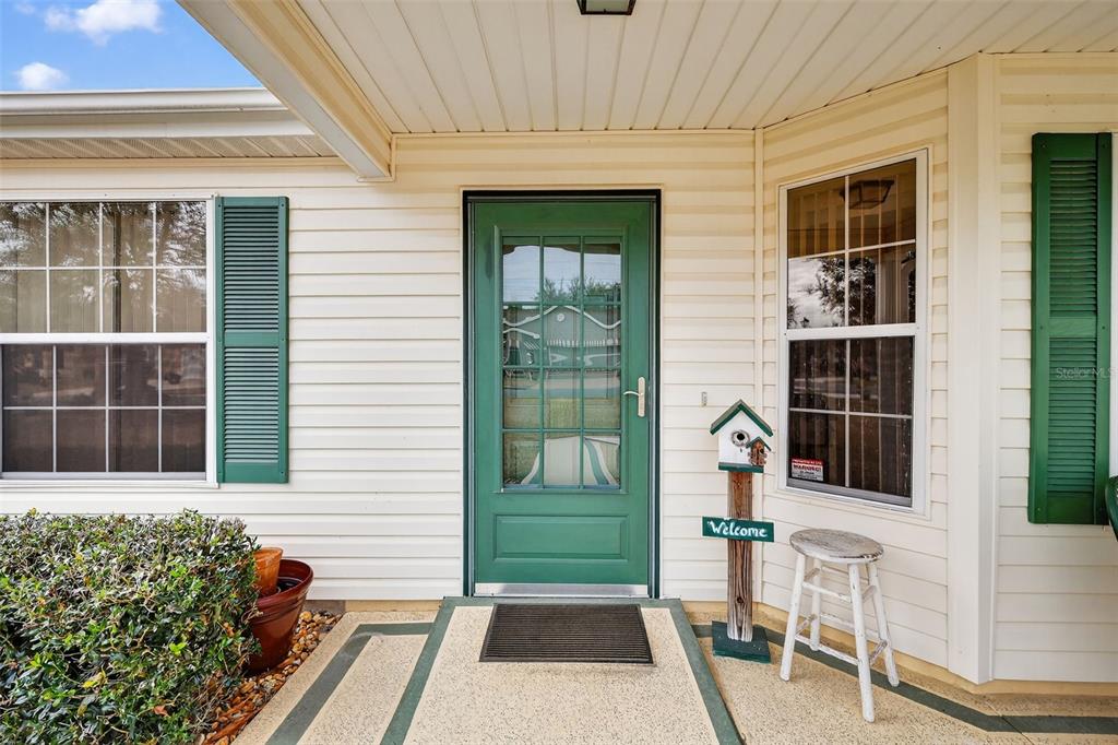 A green front door with a glass pane sits between two windows with green shutters — 648 SAN MARINO DRIVE, THE VILLAGES, FL