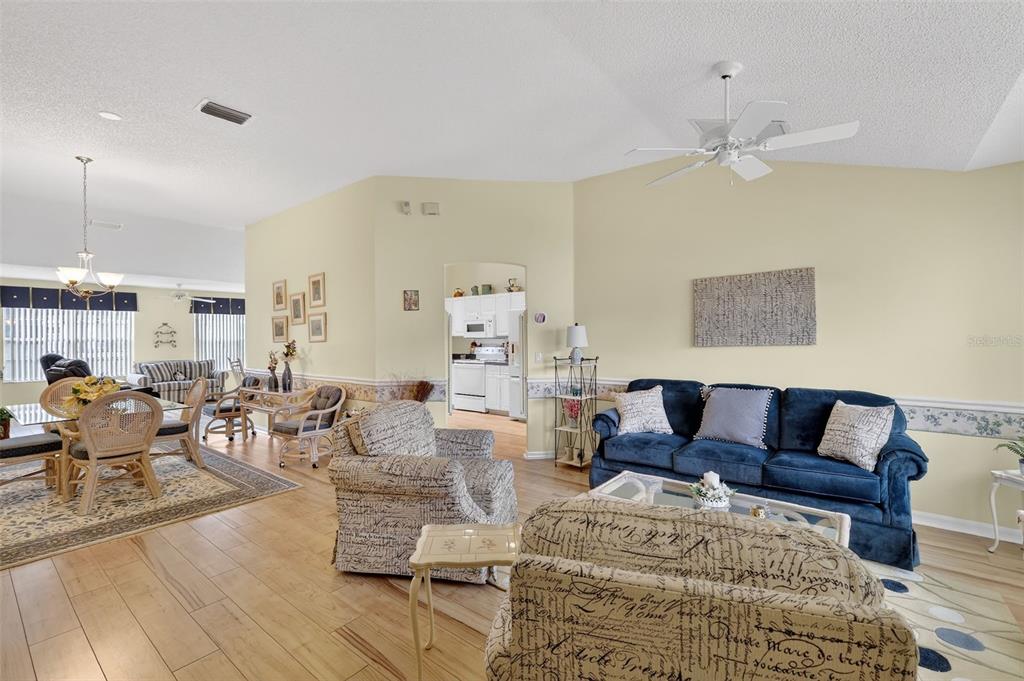 A living room with a blue sofa, patterned armchair, dining area, and light wood flooring — 648 SAN MARINO DRIVE, THE VILLAGES, FL