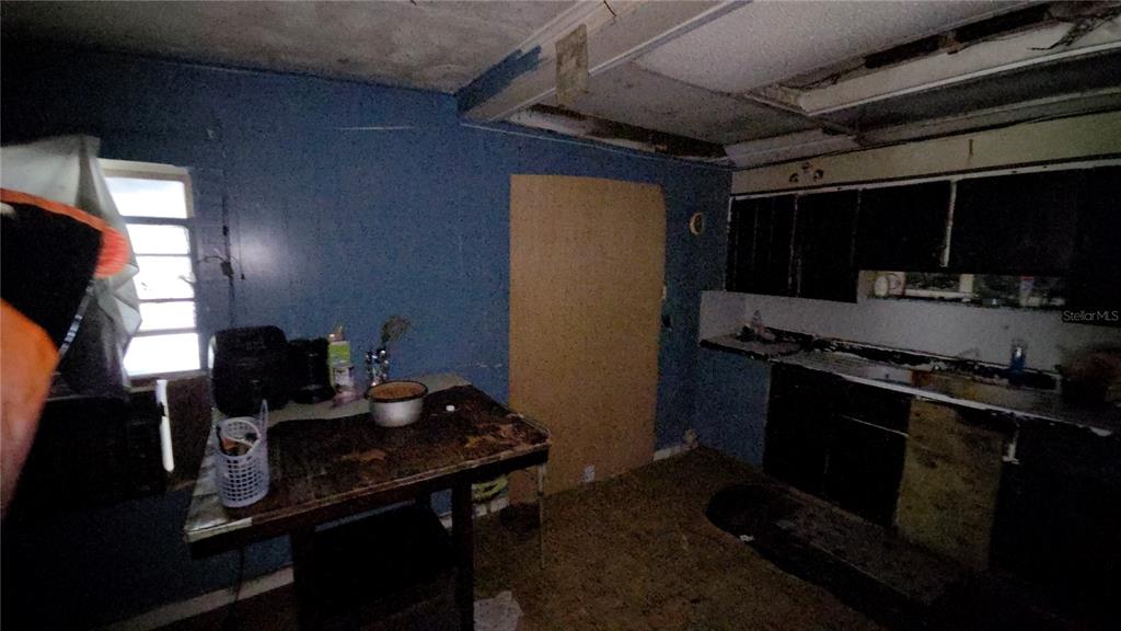 A dimly lit, unfinished kitchen features blue walls, dark cabinets, and a worn wooden table — 365 80 FOOT ROAD UNIT 4, BARTOW, FL