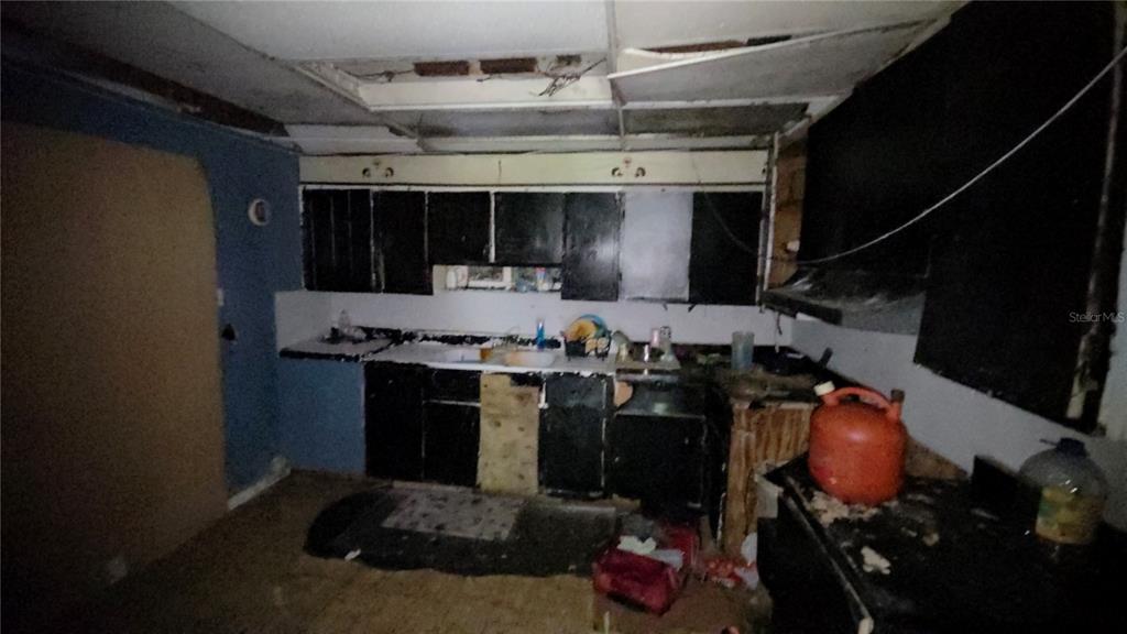 A dilapidated kitchen features dark cabinets, a damaged drop ceiling, and debris on the floor — 365 80 FOOT ROAD UNIT 4, BARTOW, FL