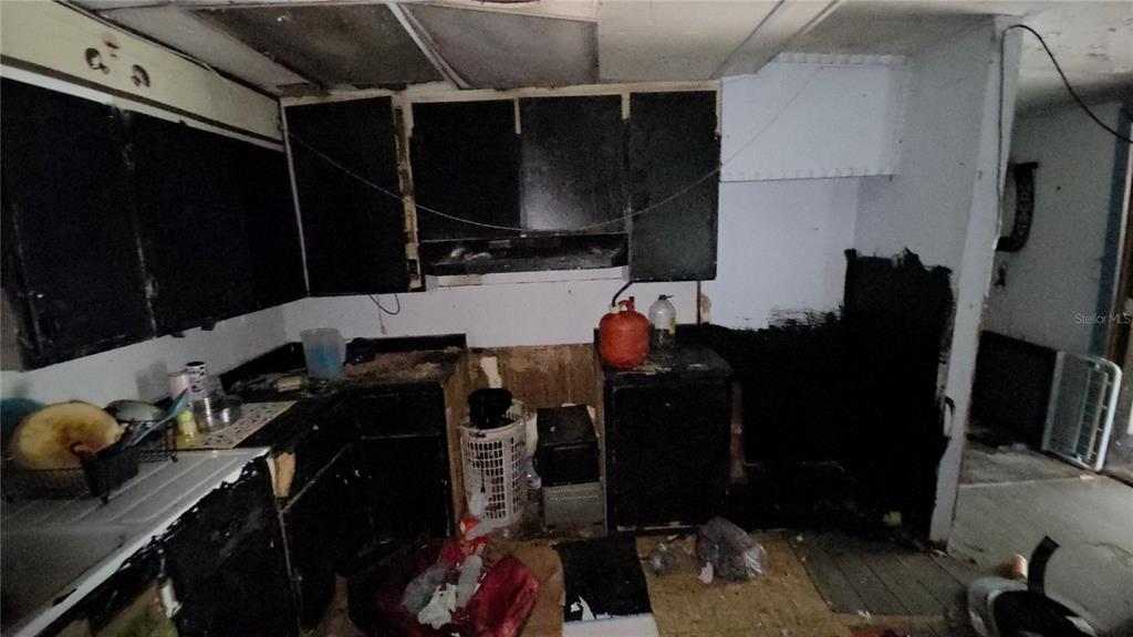 A dilapidated kitchen features dark cabinets, exposed wall studs, and significant fire or smoke damage — 365 80 FOOT ROAD UNIT 4, BARTOW, FL
