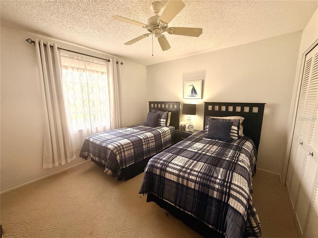 A bedroom features two twin beds with plaid bedding, a ceiling fan, and carpeted flooring — 8350 HIGH POINT CIRCLE UNIT 3, PORT RICHEY, FL