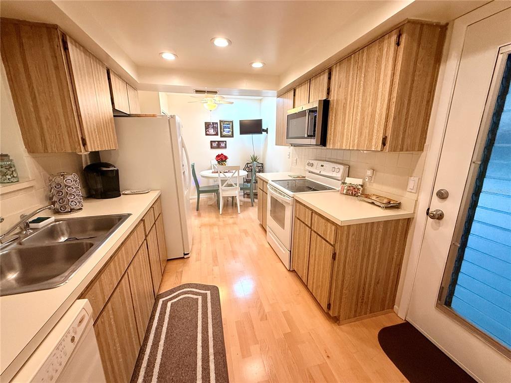 A galley-style kitchen features light wood cabinets, stainless steel appliances, and an adjacent dining area — 8350 HIGH POINT CIRCLE UNIT 3, PORT RICHEY, FL