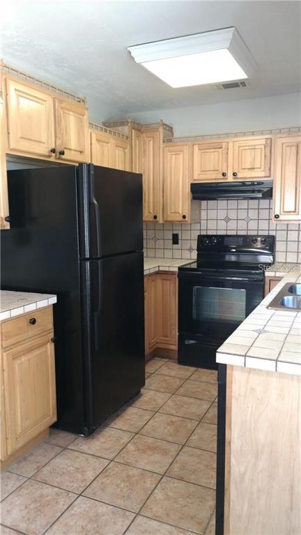 A kitchen features light wood cabinets, black appliances, and tiled countertops and flooring — 2824 WOODSIDE AVENUE, WINTER PARK, FL