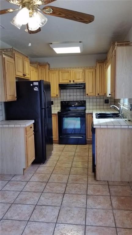 A kitchen features light wood cabinets, black appliances, and tiled countertops and flooring — 2824 WOODSIDE AVENUE, WINTER PARK, FL