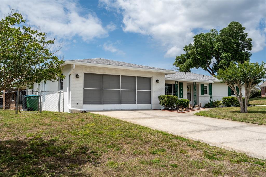 A single-story white brick house with a garage, driveway, and green shutters under a sky — 1078 ABADAN DRIVE, DELTONA, FL