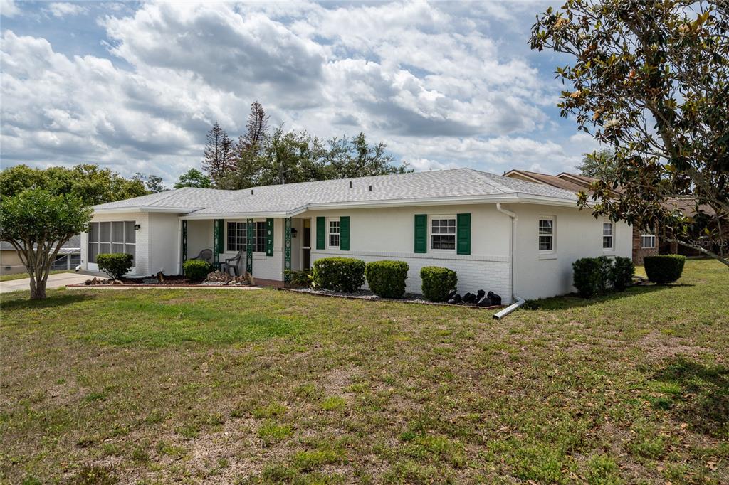 A single-story white house with green shutters and a gray shingled roof sits on grass — 1078 ABADAN DRIVE, DELTONA, FL