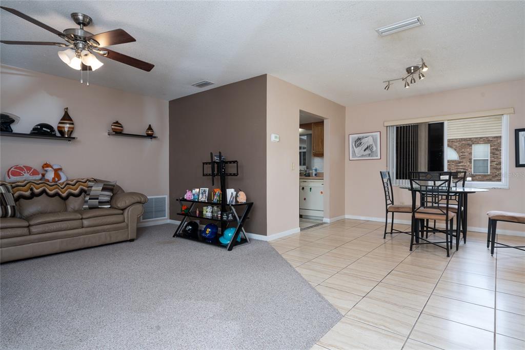 A living room with carpeted and tiled flooring features a sofa, dining set, and shelving — 1078 ABADAN DRIVE, DELTONA, FL