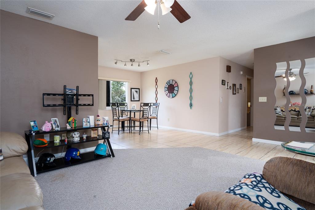 A living room with beige walls, carpeted flooring, a dining area, and a ceiling fan — 1078 ABADAN DRIVE, DELTONA, FL