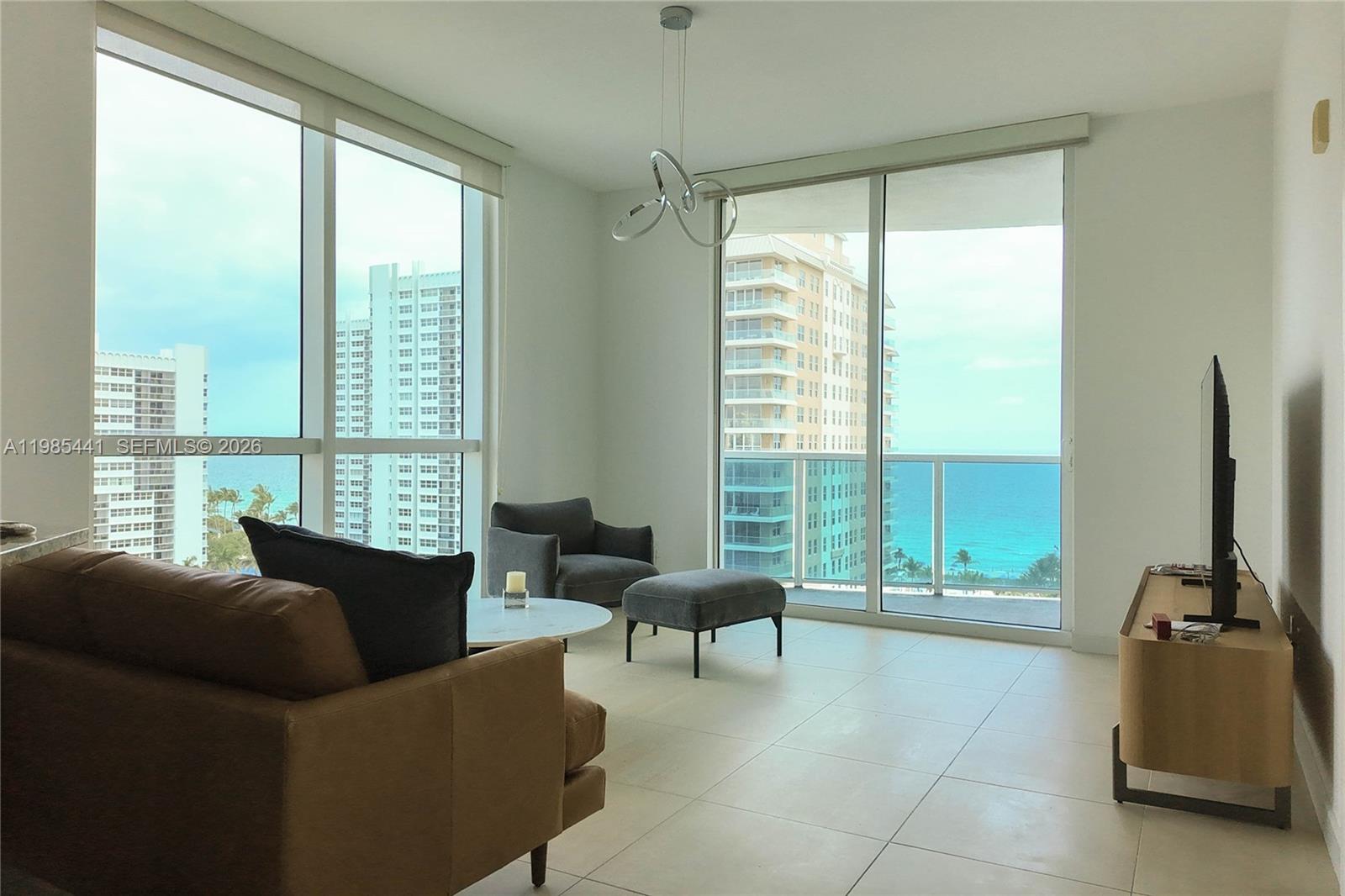 A living room features floor-to-ceiling windows with ocean views, tile flooring, and modern furniture — 1945 S Ocean Dr # 1114, Hallandale Beach FL 33009, HALLANDALE BEACH, FL
