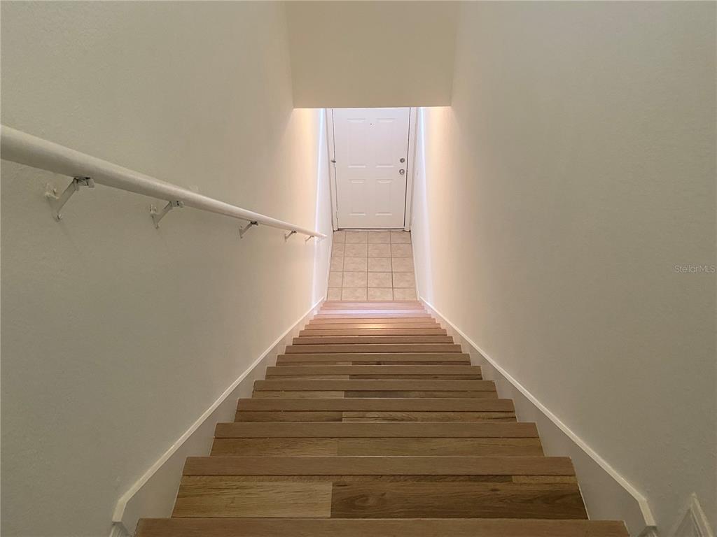 A wooden staircase with a white handrail leads down to a tiled entryway and door — 3364 WESTCHESTER SQUARE BOULEVARD UNIT 205, ORLANDO, FL