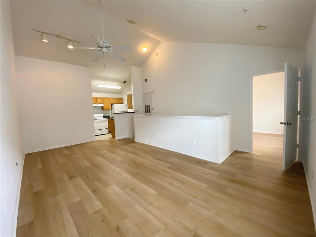 An open-concept living area features light wood-look flooring, a vaulted ceiling, and a kitchen view — 3364 WESTCHESTER SQUARE BOULEVARD UNIT 205, ORLANDO, FL