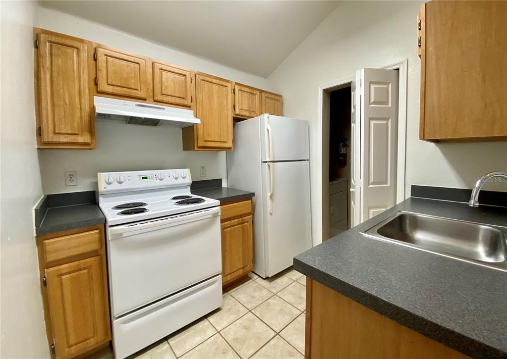 A kitchen features wood cabinets, white appliances, dark countertops, and tile flooring — 3364 WESTCHESTER SQUARE BOULEVARD UNIT 205, ORLANDO, FL