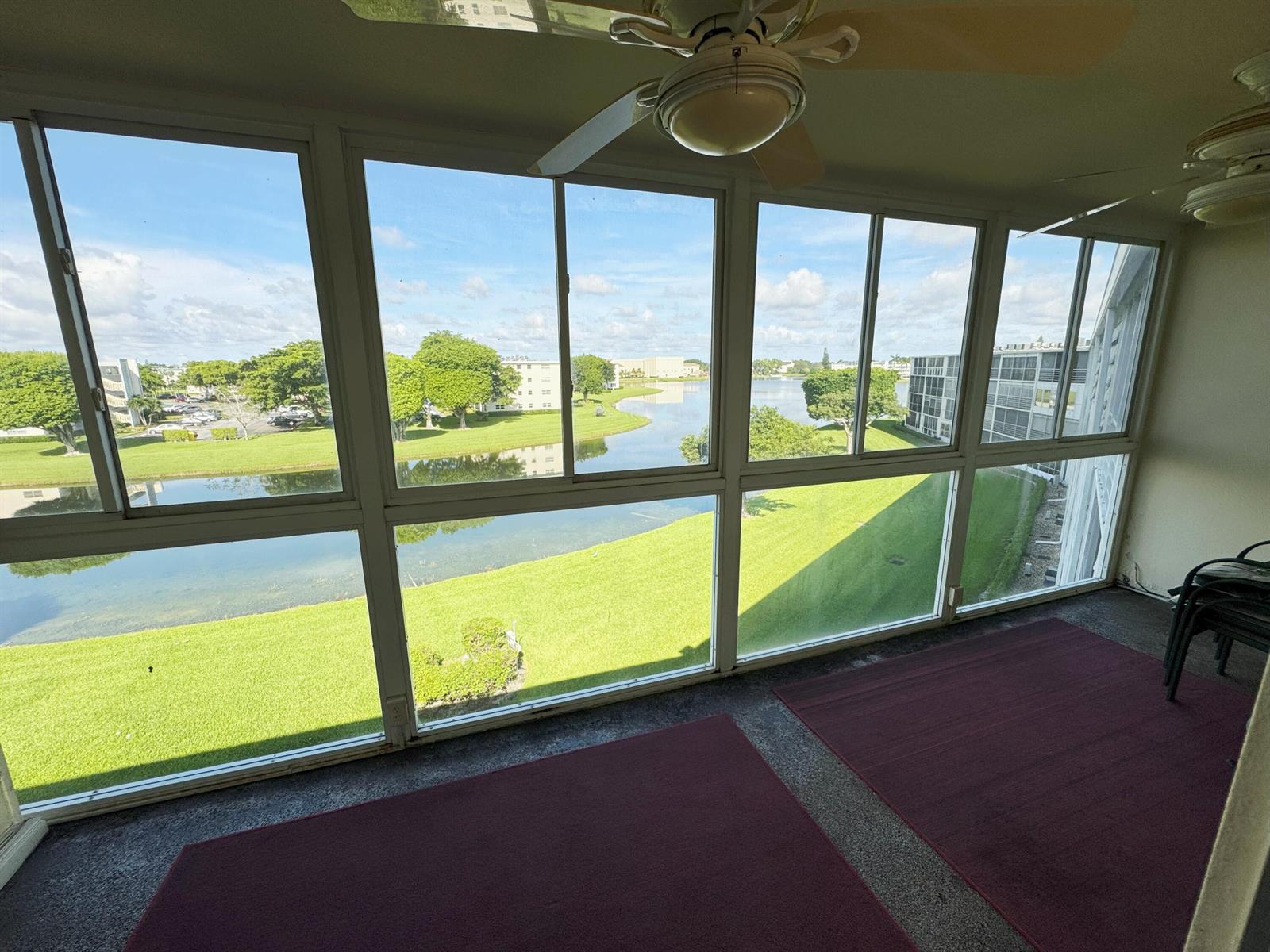 A sunroom with large windows overlooking a lake, green lawn, and nearby apartment buildings — 4075 Cornwall D, Boca Raton FL 33434, BOCA RATON, FL