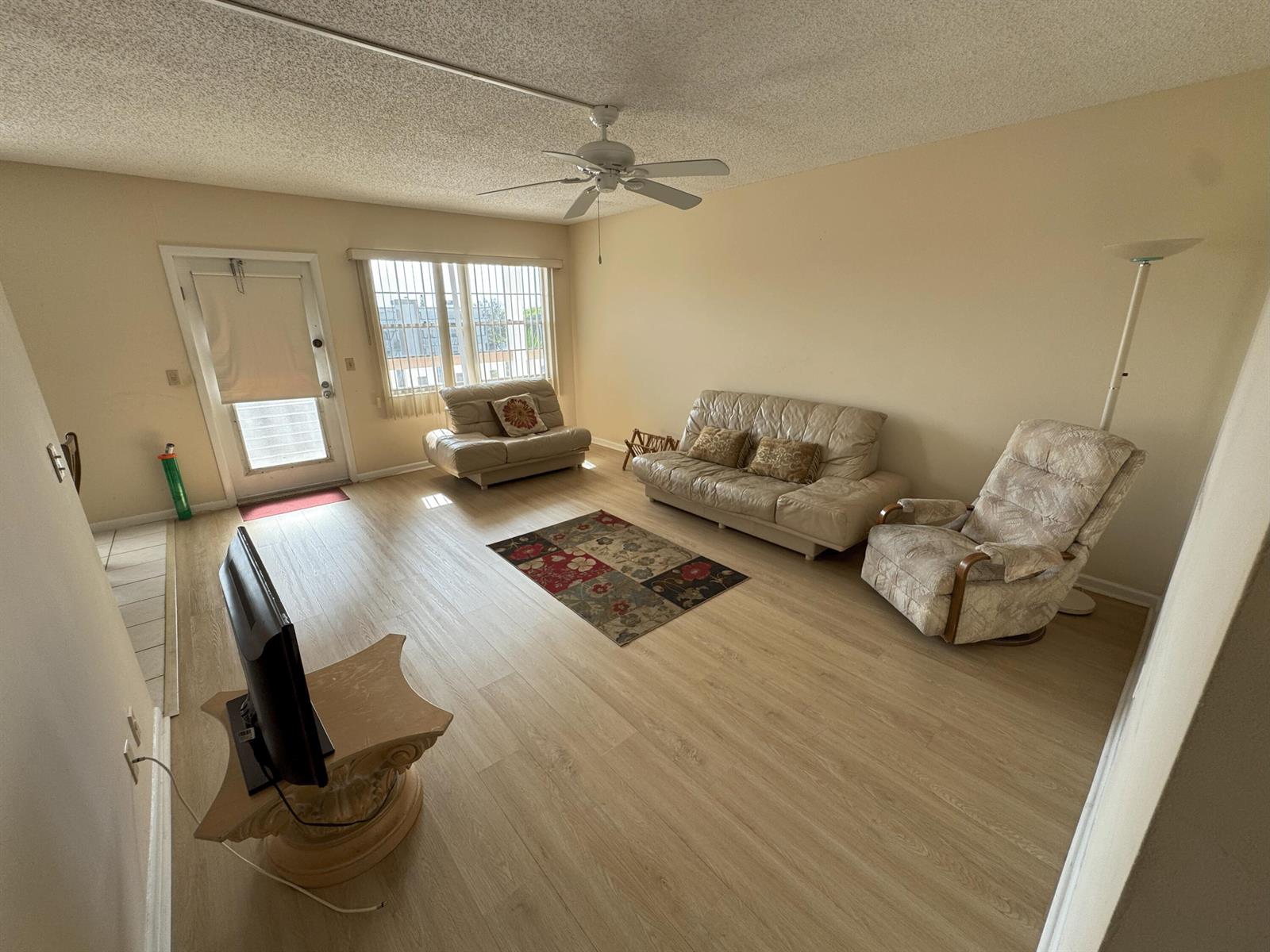 A living room features light wood-look flooring, a ceiling fan, and beige walls — 4075 Cornwall D, Boca Raton FL 33434, BOCA RATON, FL