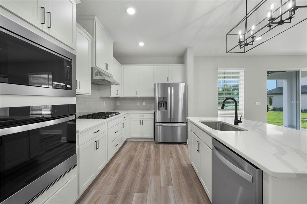 A modern kitchen features white cabinets, stainless steel appliances, a center island, and wood flooring — 7657 SOMERSWORTH DRIVE, KISSIMMEE, FL