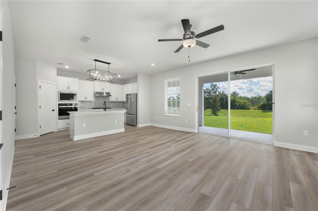 An open-concept kitchen and living area features light wood-look flooring and sliding glass doors — 7657 SOMERSWORTH DRIVE, KISSIMMEE, FL